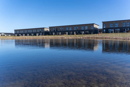 Billede af Remmerslund Skovby, med boliger i baggrunden og en sø i forgrunden.