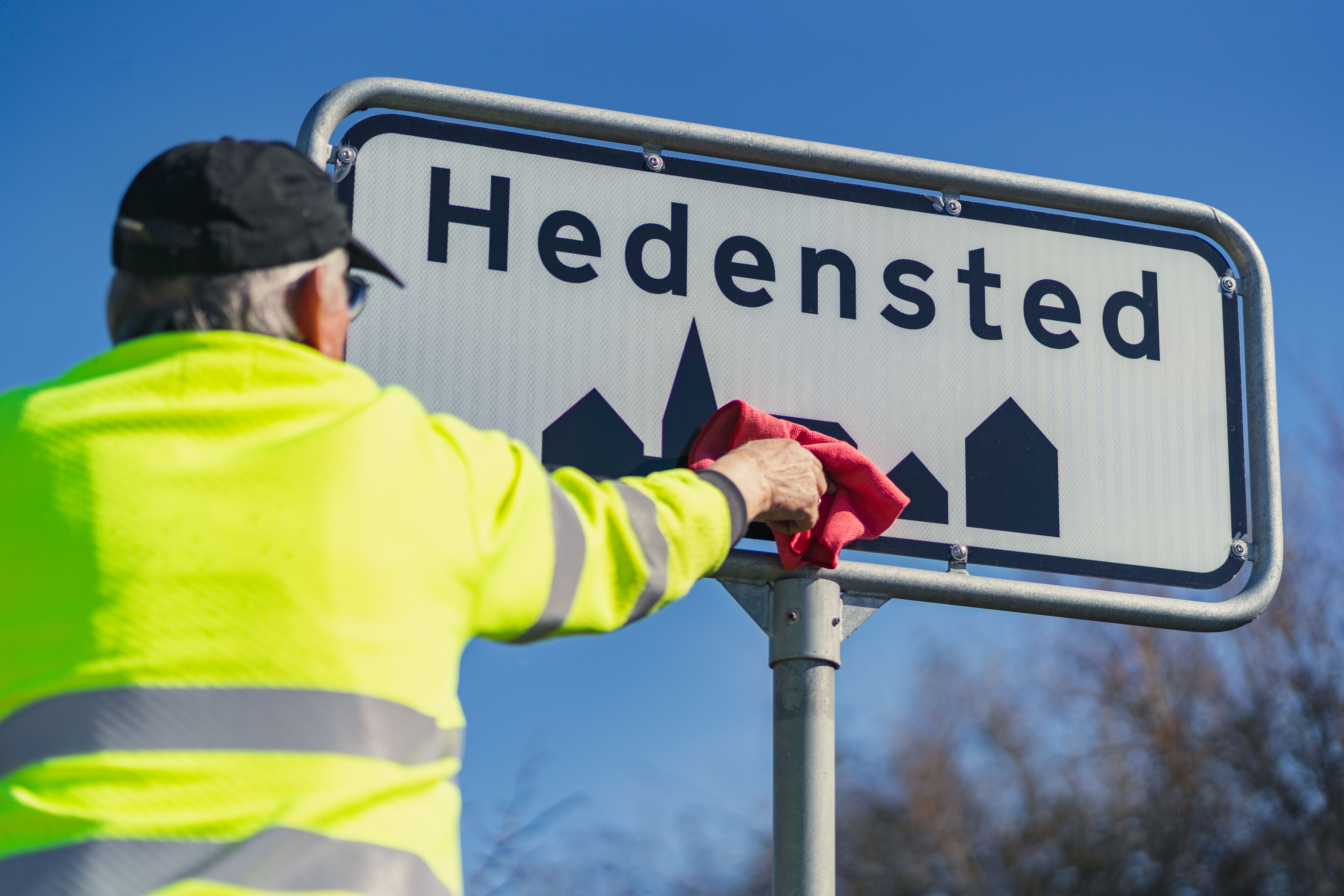 En kommunaltansat pudser et byskilt i Hedensted.