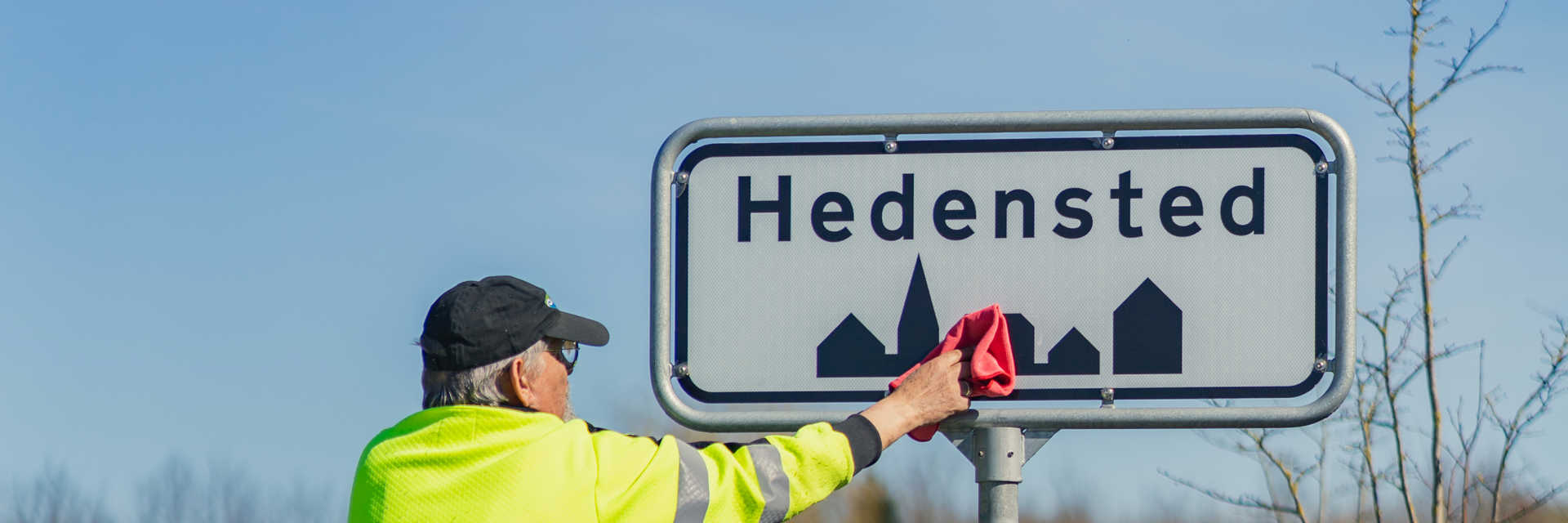 En kommunaltansat pudser et byskilt i Hedensted.